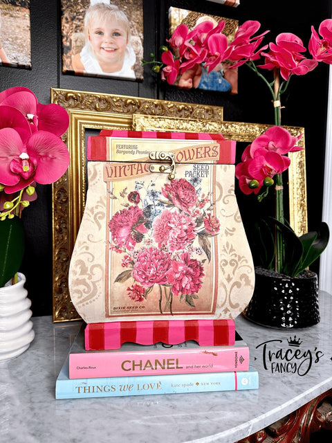 A decorative setup featuring a lamp-shaped floral art piece with "Vintage Flowers" text, framed photos, and pink orchids. Below are two books: "Chanel," and "Things We Love."