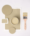 A paintbrush with green paint lies next to a jar filled with the same color. Green paint swatches and round samples are arranged around the jar on a light background.