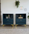 Matching modern nightstands painted in a deep blue finish with gold legs and hardware, styled with books, plants, and decor in a bright minimalist room.