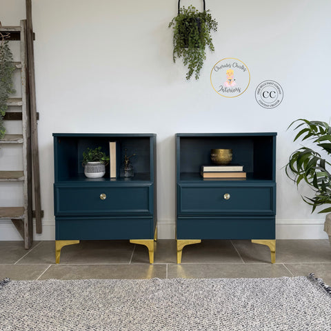Matching modern nightstands painted in a deep blue finish with gold legs and hardware, styled with books, plants, and decor in a bright minimalist room.