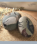 Bluish teal painted faux eggs with the Elegant Avian Flora Transfer applied on them. Staged on a woven placemat next to faux eucalyptus.