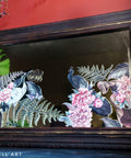 Elegant Avian Flora Transfer applied on a mirror. Mirror frame is painted with a dark purplish black. Staged against a red wall.