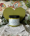 Green painted wooden heart with a jar of Everglades in front of it. Staged on crocheted lace with faux flowers and greenery.