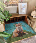 A wooden desk with an open compartment reveals a painted image of a fox with flowers on its head, set against a blue background. On top of the desk are framed butterfly art and a potted plant. The wall behind it has sun and floral decorations.
