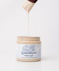 A paintbrush dripping beige paint above an open jar labeled "Silk All-in-One Mineral Paint, French Villa" against a plain white background.