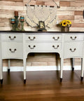 Grayish white painted dresser makeover with dark brown feet and top and bronze pulls. Staged with candlesticks, a picture frame and sunflowers on top.