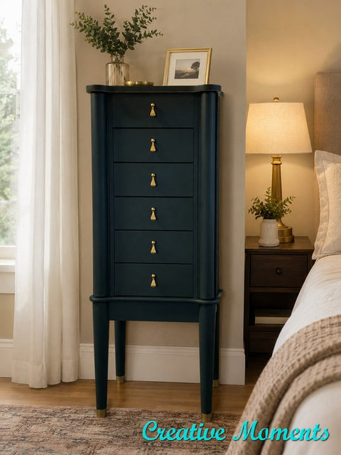 Dark green jewelry armoire with gold knobs in a bedroom setting, featuring 'Creative Moments' text.