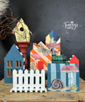 Five little painted house cutouts and a yellow birdhouse along with a white picket fence cutout. Mr. Toad's Transfer has been applied to the front of the house and birdhouse.