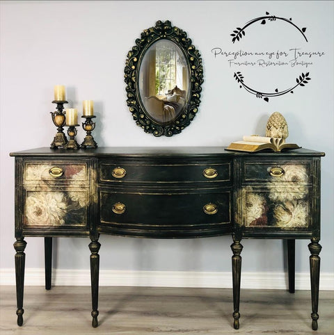 Vintage-style sideboard with floral patterns and ornate drawer handles, below an oval mirror. Candles and a decorative pineapple sit atop. A watermark in cursive script decorates the wall.