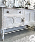 Baja Gray Silk All-In-One paint is perfect for painting kitchen cabinets, bathroom cabinets and painting furniture. This image shows a beautiful whitewash using Baja Gray Silk All-In-One Mineral Paint on a 3 door cabinet. The piece is staged with pine cones, a snow globe, Christmas stockings and a Christmas tree against shutter doors.