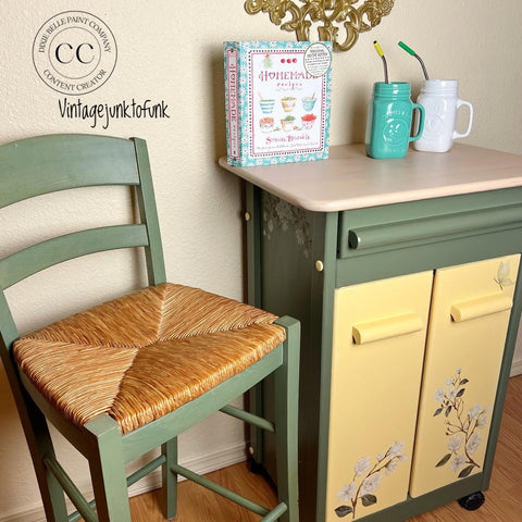 Cactus Silk All-In-One paint is perfect for painting kitchen cabinets, bathroom cabinets and painting furniture.
A kitchen cart paired with a chair both painted in Cactus Silk All-In-One Mineral Paint® with the doors painted from the Chalk Mineral Paint line in Rebel Yellow as well as the Belles and whistles Magnolia garden transfer on the doors and the top has Voodoo gel stain in Au naturel. Staged with two mason jar cups blue and white with metal straws and a "HOMEMADE RECIPES" cookbook.
