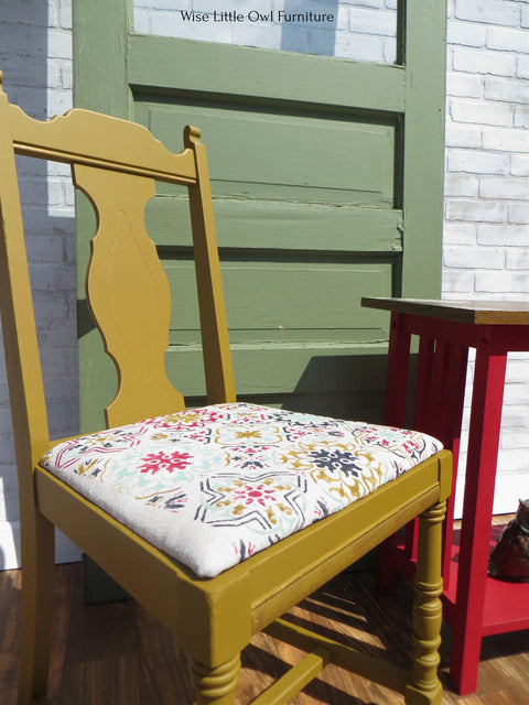 Mojave Silk All-In-One paint is perfect for painting kitchen cabinets, bathroom cabinets and painting furniture. Yellow Silk painted chair with a colorful fabric on top. Staged outside by a green door and red end table.