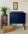 Nautical Silk All-In-One paint is perfect for painting kitchen cabinets, bathroom cabinets and painting furniture. Dark blue chalk painted cabinet with gold hardware. Staged next to a potted plant with a pillow.