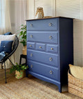 Nautical Silk All-In-One paint is perfect for painting kitchen cabinets, bathroom cabinets and painting furniture. Dark blue painted dresser with gold hard ware. Staged in a bedroom with plants and wicker basket.