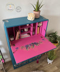 Prickly Pear Silk All-In-One paint is perfect for painting kitchen cabinets, bathroom cabinets and painting furniture.  Blue chalk painted secretary desk with pink chalk painted inside. Tropical leaves rub on transfer on the front and inside the desk. Staged with books, and candles and a plant.