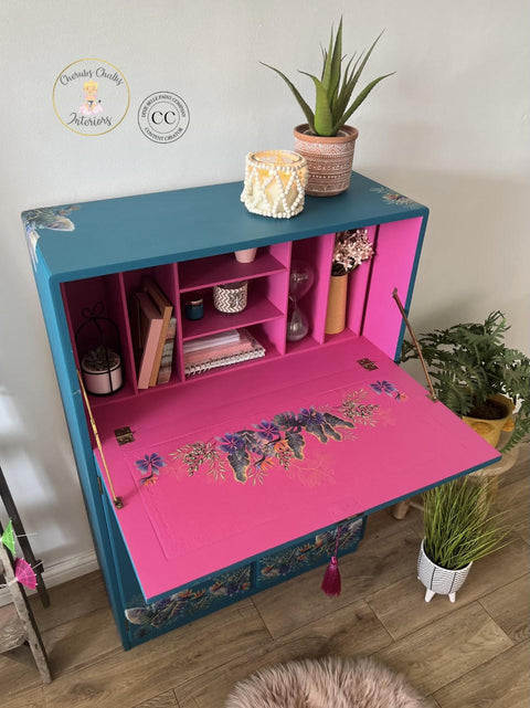 Prickly Pear Silk All-In-One paint is perfect for painting kitchen cabinets, bathroom cabinets and painting furniture.  Blue chalk painted secretary desk with pink chalk painted inside. Tropical leaves rub on transfer on the front and inside the desk. Staged with books, and candles and a plant.