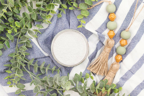 Silk All-In-One Mineral Paint Pristine Clean Concentrate. Open top view of Pristine clean concentrate. Staged with plants, a blue and white stripe towel, and wood and green beads.