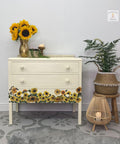 Sun Kissed Silk All-In-One paint is perfect for painting kitchen cabinets, bathroom cabinets and painting furniture.
Chest of drawers painted in Sun Kissed Silk All-In-One paint with the Sunflower transfer along the bottom last drawer. Staged with a metal vase with sunflower, greenery and woven baskets. In a gray patterned floor and white wall.