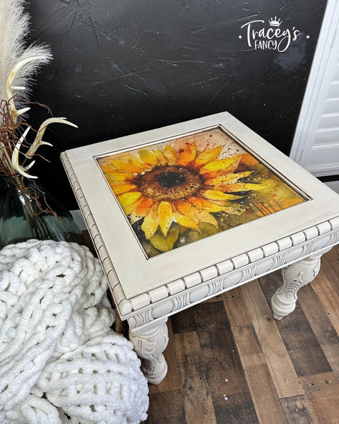 A vintage-style painted coffee table with an ornate Sunny Daze A1 Rice Decoupage Paper design on the tabletop, set against a dark wall with a cozy chunky knit blanket on the side.