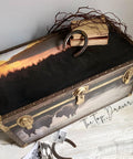 Belles and Whistles Tatanka - A1 Rice Decoupage Paper is a simple way to visually enhance any surface of your project! Large chest with leather on the edges and gold hinges and clasps. The Tatanka Rice Decoupage Paper has been applied to the top of the chest. There is newspaper clippings on the floor in front of the chest along with a rusty horseshoe.