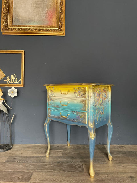 Blue Moon Terra Clay Paint provides endless possibilities for your imagination and can be used on wood, canvas, tile, fabric and more!
Bedside table with ombre design going from yellow to a tan fading into a Cerulean Blue Terra Clay Paint blending in to  Blue Moon Terra Clay Paint. Using gold hardware and gold on woodwork. Staged In front of black wall and gold picture frames.