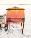 Bougainvillea Terra Clay Paint provides endless possibilities for your imagination and can be used on wood, canvas, tile, fabric and more!
Secretary desk painted with Marigold, Daffodil & Bougainvillea Terra Clay Paint with Gold Gilding Waxing along the hardware. Staged along a white wall.