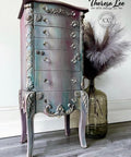 Bougainvillea Terra Clay Paint provides endless possibilities for your imagination and can be used on wood, canvas, tile, fabric and more!
Chest of drawers painted with Bougainvillea Terra Clay Paint and a blend of colors to give it a goth look. Staged with a large jug with feathers inside on gray wood floors in front of white wall.