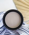 Desert Tan Terra Clay Paint provides endless possibilities for your imagination and can be used on wood, canvas, tile, fabric and more!
Here, you are looking directly over the Desert Tan Terra Clay Paint container.  There is fabric on the white table under and around the paint.  There is blue and white stripes and dashes on the fabric.  There is also a dried out palm frond laying next to the paint container.
