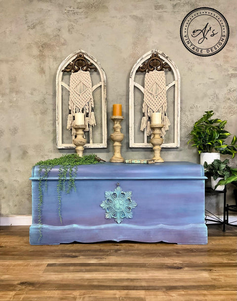Elderberry Terra Clay Paint provides endless possibilities for your imagination and can be used on wood, canvas, tile, fabric and more! Blue/purple clay painted chest with a large string of faux string of pearls placed on top. Along with three large candlesticks. Two large arches on the wall with macrame inside. Two white pots with large plants inside on a black plant stand.