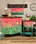 Elderberry Terra Clay Paint provides endless possibilities for your imagination and can be used on wood, canvas, tile, fabric and more! Pink and green clay painted furniture with a flower garden scape painted on the fronts. Basket with multicolor flowers, yellow painted owl figurine, and candlestick on top of the dresser. Yellow vase of multicolor flowers on top of the end table. Canvas with the same painted flower garden scape hung on the wall.