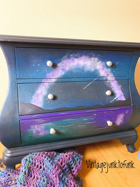 Galaxy Terra Clay Paint provides endless possibilities for your imagination and can be used on wood, canvas, tile, fabric and more! A side table painted with Galaxy Terra Clay Paint that has a handpainted scene that looks like the night sky.