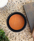 Marigold Terra Clay Paint provides endless possibilities for your imagination and can be used on wood, canvas, tile, fabric and more! Orange can of Terra Clay artisan paint sitting on a wicker table cover with a book, wood cutting board, and ivy plant around it.