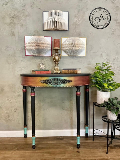 Onyx Terra Clay Paint provides endless possibilities for your imagination and can be used on wood, canvas, tile, fabric and more! End table painted Rainbow Ombre on the front with Terra Clay paint and black clay paint on the legs. Staged with book with candle sticks and candles on top and some plants in white pots besides it.