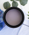 Wisteria Mist Terra Clay Paint provides endless possibilities for your imagination and can be used on wood, canvas, tile, fabric and more!  Top view of an open container of Wisteria Mist Terra Clay Paint sitting on a white cloth with purple flowers to the left of the container and greenery to the right and back of the container.