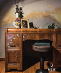 Dark wood desk in front of a faux marble wall, with the Timeless Petals Transfer applied on the drawers. Wooden barstool pulled up to the desk with a book resting on it. Staged with a lamp, picture frame, open book, and pothos plant on top.