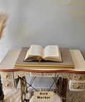 Decorative table with an open book on top, featuring intricate designs and a gold marker label.