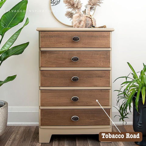 A wooden dresser with five drawers stands between two plants. On top, there's a round mirror and a decorative vase. A label that reads "Tobacco Road" points to the dresser's color.