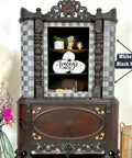 An ornate vintage cabinet with open doors displaying a decorative platter and figurines. The exterior has a checker pattern and intricate woodwork. A nearby vase holds decorative branches and pink flowers. A label reads "White Magic and Black Magic."