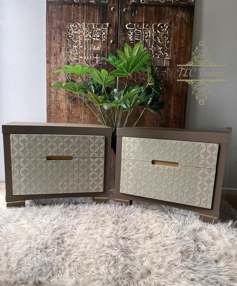 Two modern nightstands with geometric patterned drawers and inset handles are placed on a fluffy beige rug. A tall green plant and a carved wooden door are in the background.