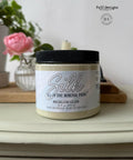 A jar of Silk All-in-One Mineral Paint, labeled "Wicklow Glen," sits on a light-colored table. In the background, there is a pink rose in a vase and blurred decorative items.