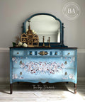 WoodUBend Applique #1339 (Set of 2) is the perfect mouldable embellishment for any project! Image of one Applique #1339 applied to light blue multi toned chalk mineral painted dresser. The appliques and hardware are finished in a bronze color. The dresser is also finished with a floral pattern painted on the front.