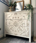 WoodUBend Applique #2150 (Set of 2) is the perfect mouldable embellishment for any project!
A white dresser with intricate woodwork design in the center of the dresser with the Applique #2150 (Set of 2) included. Staged on top of the piece is greenery, framed mirrors and a stack of books with a black candle.