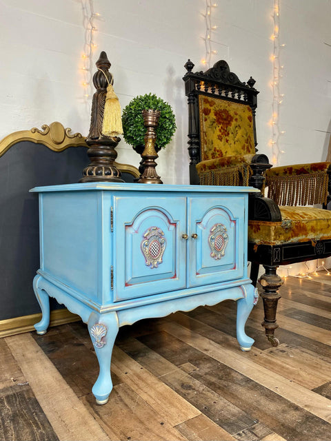 WoodUBend Applique #2447 (set of 2) is the perfect mouldable embellishment for any project!
A blue end table with Applique #2447 (set of 2) on the tops of both legs. Staged next to a yellow fabric chair, on top of the piece are bronze statues.