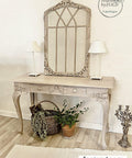 WoodUBend Applique #6069 (Set of 2) 
This applique is quite big.  This picture is of a table with a large mirror in the center.  The mirror is leaning up against the wall that the table is in front of. The table has two, white lamps which are on either side of the mirror.  There are 3 Appliques on the mirror; two on the bottom corners and one at the very top.  Everything is painted  with Moon Beam Terra Paint.  It is staged with plants and a candle opera.
