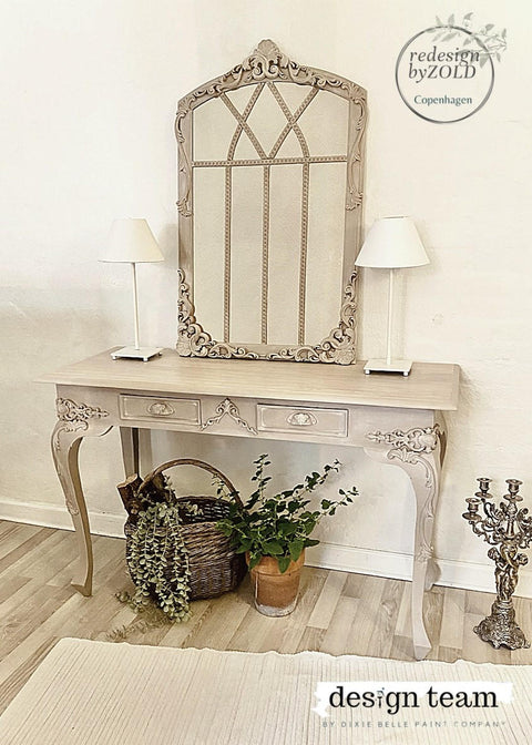 WoodUBend Applique #6069 (Set of 2) 
This applique is quite big.  This picture is of a table with a large mirror in the center.  The mirror is leaning up against the wall that the table is in front of. The table has two, white lamps which are on either side of the mirror.  There are 3 Appliques on the mirror; two on the bottom corners and one at the very top.  Everything is painted  with Moon Beam Terra Paint.  It is staged with plants and a candle opera.