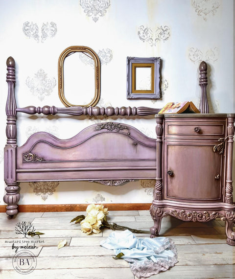 WoodUBend Corner Applique #2093 (set of 2) 
There is a night table and a headboard painted rose and lavender and antiqued.  There are ornate appliques on the bottom of the night table.  There are two picture frames hanging on the back wall that is white and yellow.  A bouquet of pale, yellow flowers lay on the whitewashed wood floor.  In front of the flowers is a light blue skirt tossed on the floor.