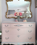 WoodUBend Fleur-de-lis Applique #2443 (set of 2) is the perfect mouldable embellishment for any project!
A pink dresser with the Fleur-de-lis Applique #2443 in silver going down the center of the drawers. Staged with a glass vase with pink flowers and a chandelier candle holders with flowers in the cups. A large gold framed mirror hanging above the dresser.