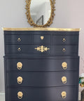 WoodUBend Fleur-de-lis Applique #2443 (set of 2) is the perfect mouldable embellishment for any project!
A black chest of drawers with the top, legs and as well as the hardware in gold. The Fleur-de-lis Applique #2443 on the bottom trim of the piece. Staged with a gold oval framed mirror.