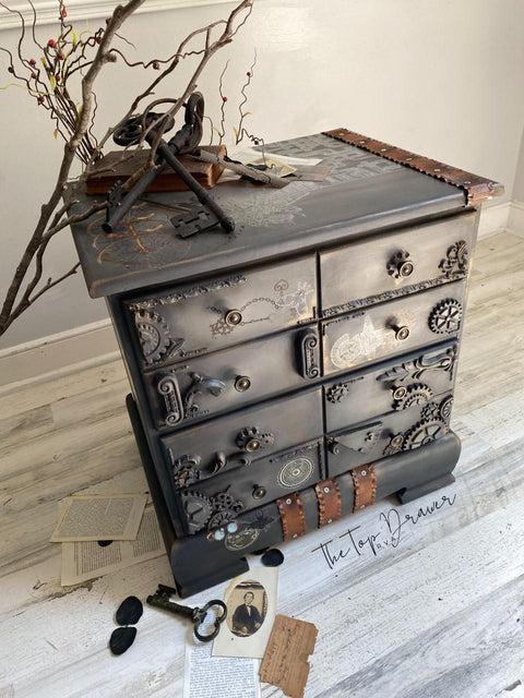 WoodUBend Trim #TR37 is the perfect mouldable embellishment for any project!  A brown chalk painted dresser with brown metal strips, brown gears and WoodUBend attached to the front.  Staged with large black keys and branches.