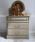 WoodUBend Trim #TR716 (Set of 2) is the perfect mouldable embellishment for any project!  A brown chalk painted night stand with gold handles.  WoodUbend is applied to the bottom front of the night stand.  The night stand is staged on a whitewashed wood floor, in front of a gray wall with white wood trim.  A brown wooden bird nest, brown branches and an oval picture of a young girl sit on top of the night stand.